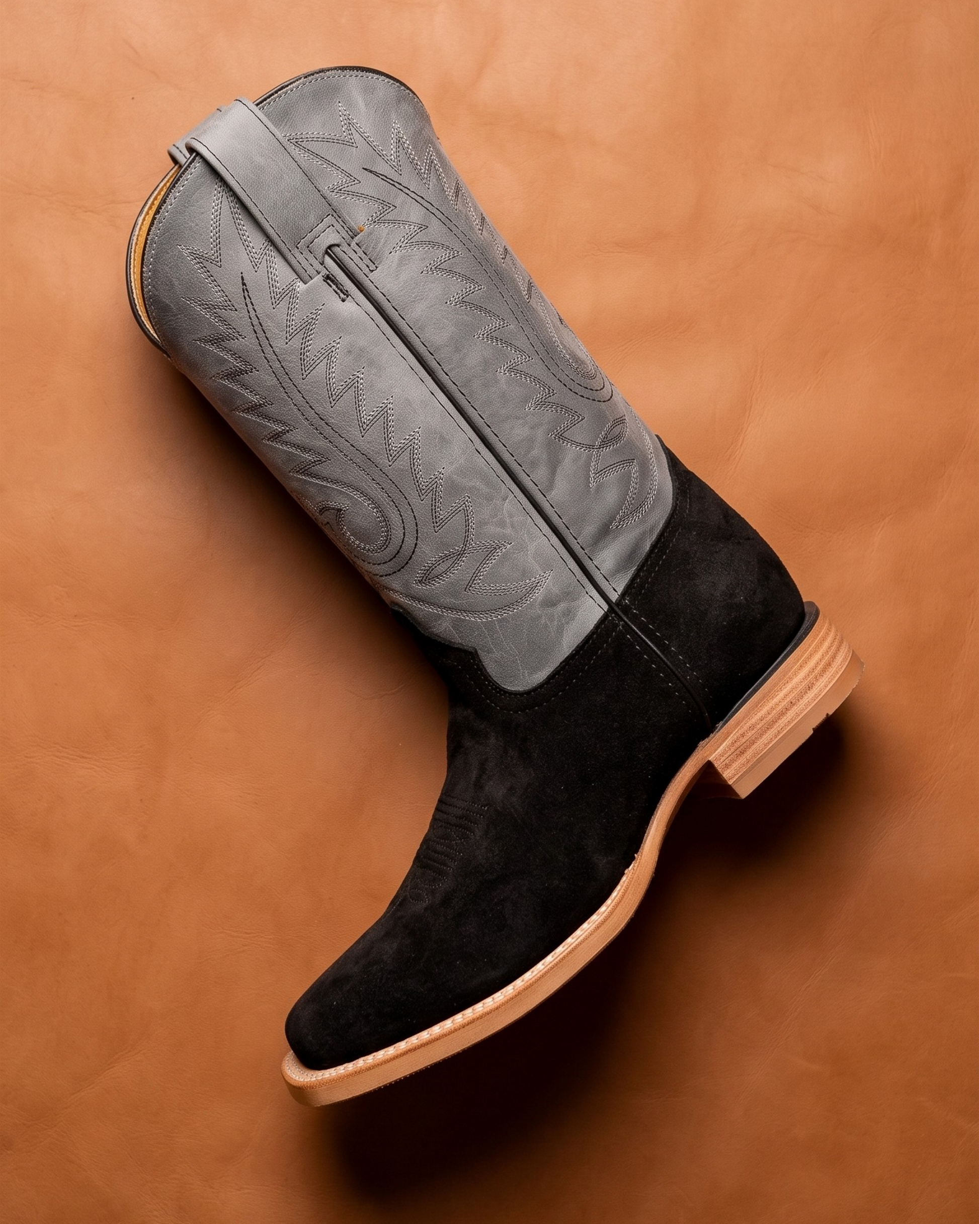 Black suede boot with gray insole on a brown leather background