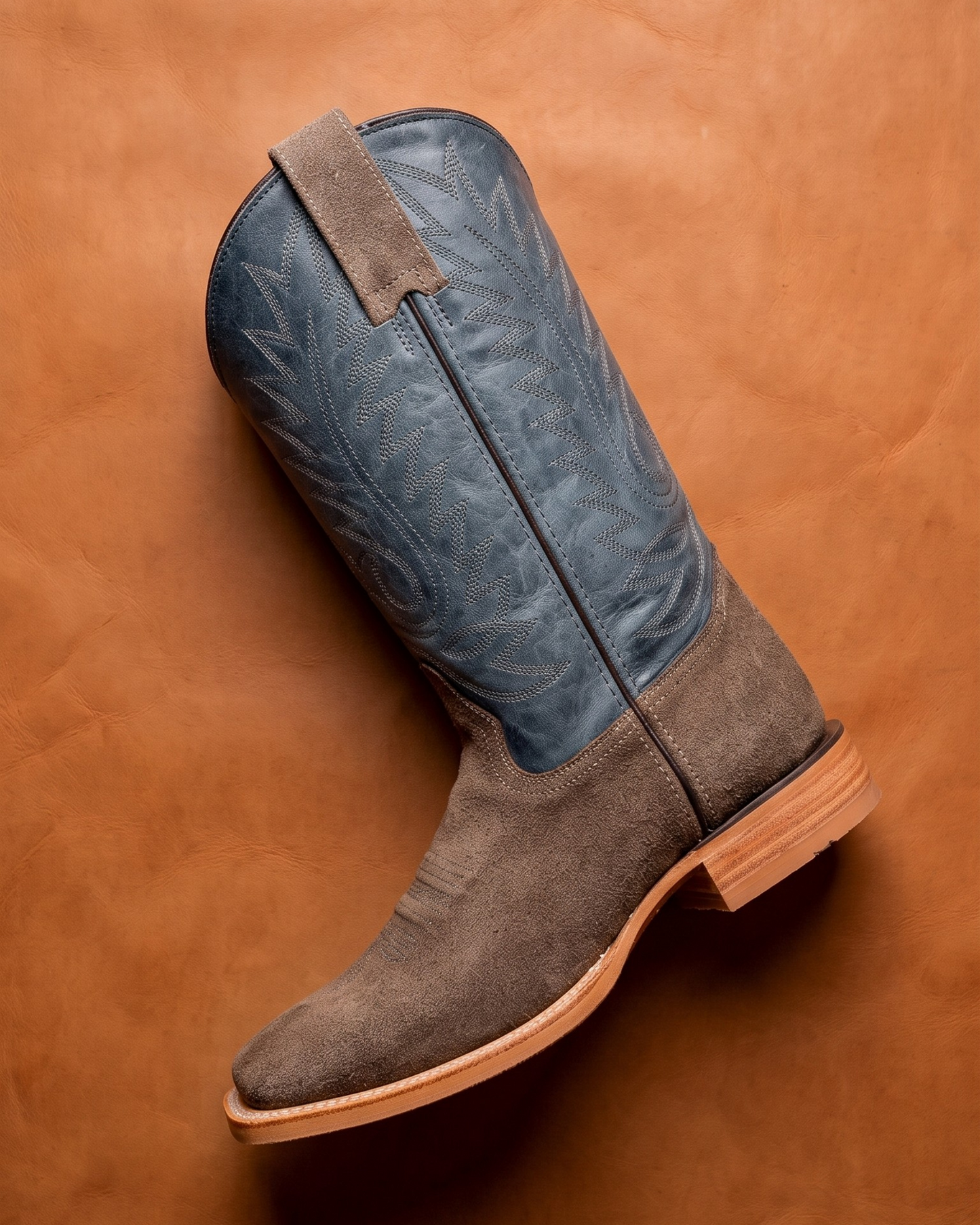 Gray and blue cowboy boot on a brown leather background